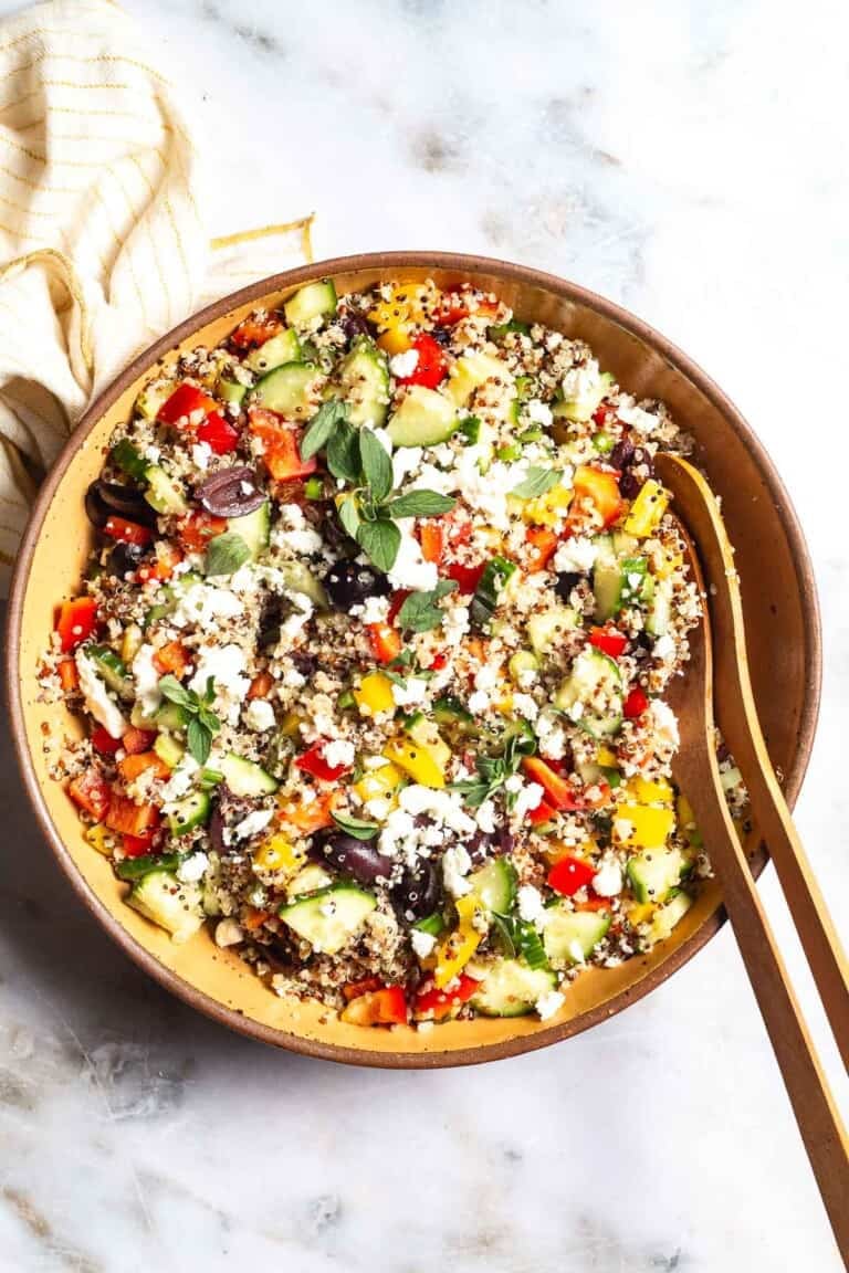 An overhead photo of quinoa salad in a large bowl with wooden serving utensils next to a cloth napkin.