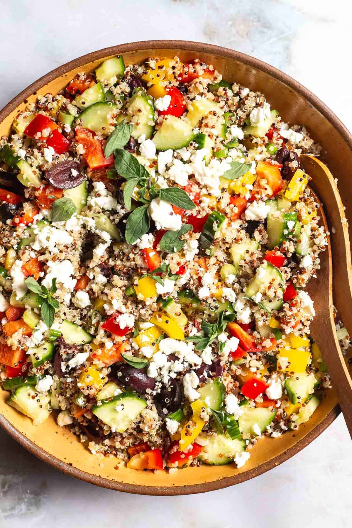 An overhead photo of quinoa salad in a large bowl with wooden serving utensils.