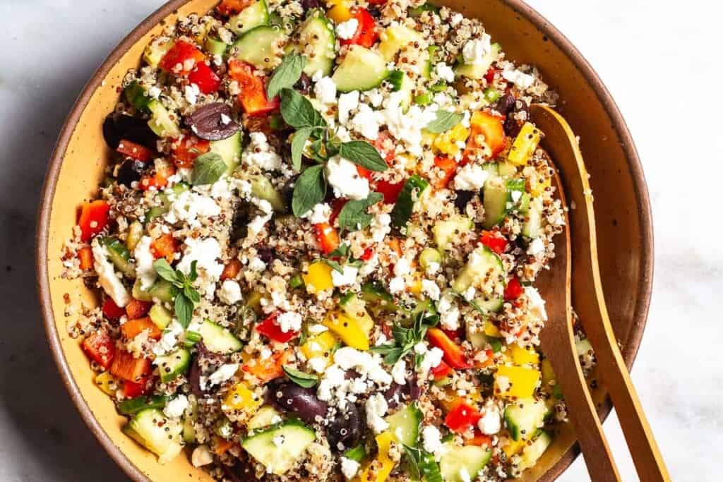 An overhead close up of quinoa salad in a large bowl with wooden serving utensils.