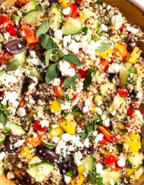 An overhead close up of quinoa salad in a large bowl with wooden serving utensils.