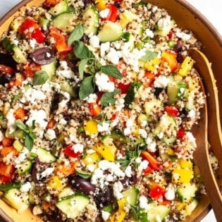 An overhead close up of quinoa salad in a large bowl with wooden serving utensils.