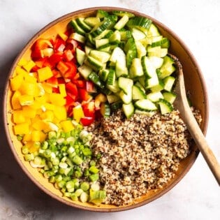 the ingredients for the quinoa salad in a serving bowl just before being mixed together with a wooden spoon.