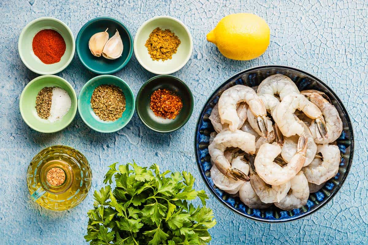 Ingredients for sheet pan shrimp including lemon, olive oil, garlic, sweet paprika, oregano, coriander, cumin, Aleppo pepper, salt, pepper, shrimp and parsley.
