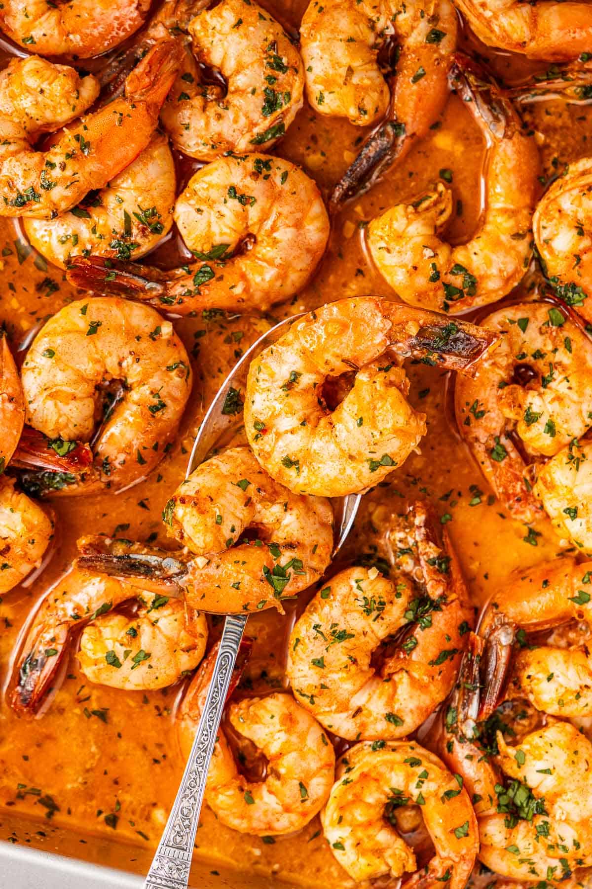 an overhead photo of the sheet pan shrimp in sauce, with two shrimps being lifted with a spoon.