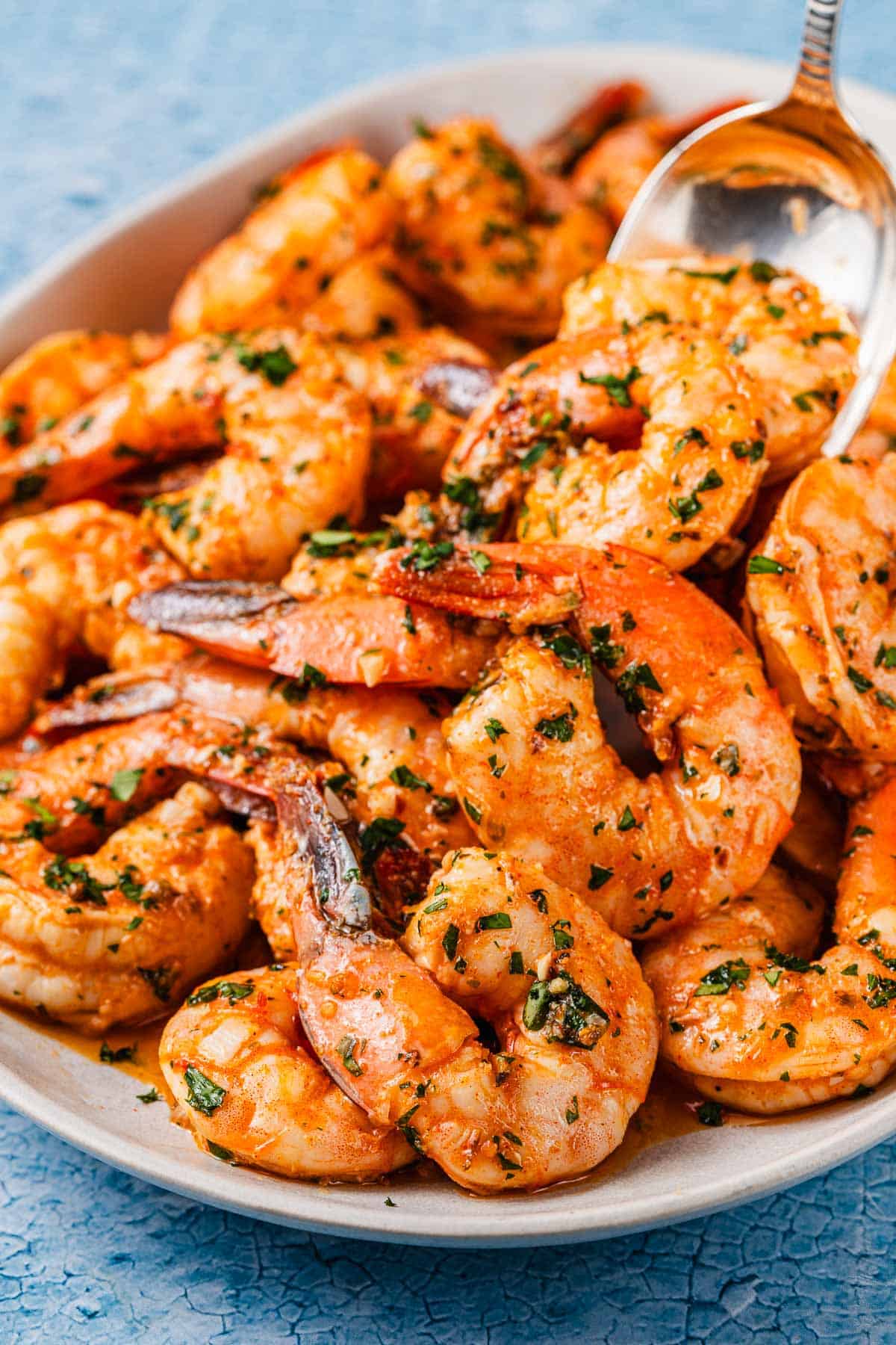 sheet pan shrimp in sauce on a serving platter, with one being lifted with a spoon.