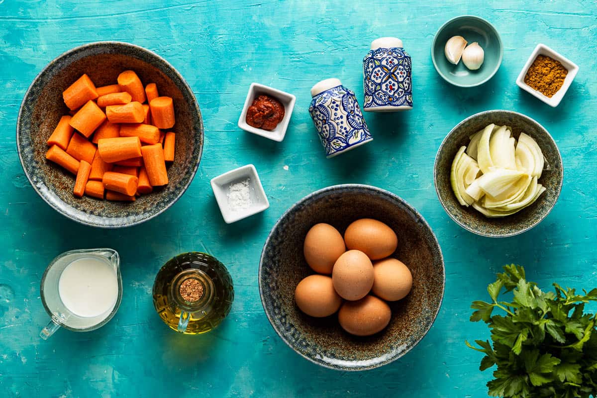 ingredients for tunisian style baked frittata with carrot including eggs, carrots, onion, parsley, milk ras el hanout, baking powder, salt, pepper, garlic, olive oil and harissa.