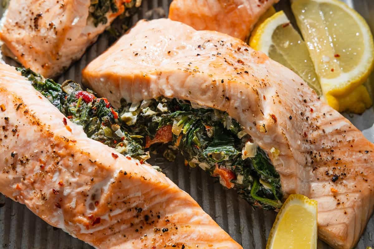 A close up of cooked stuffed salmon fillets on a baking sheet with lemon wedges.