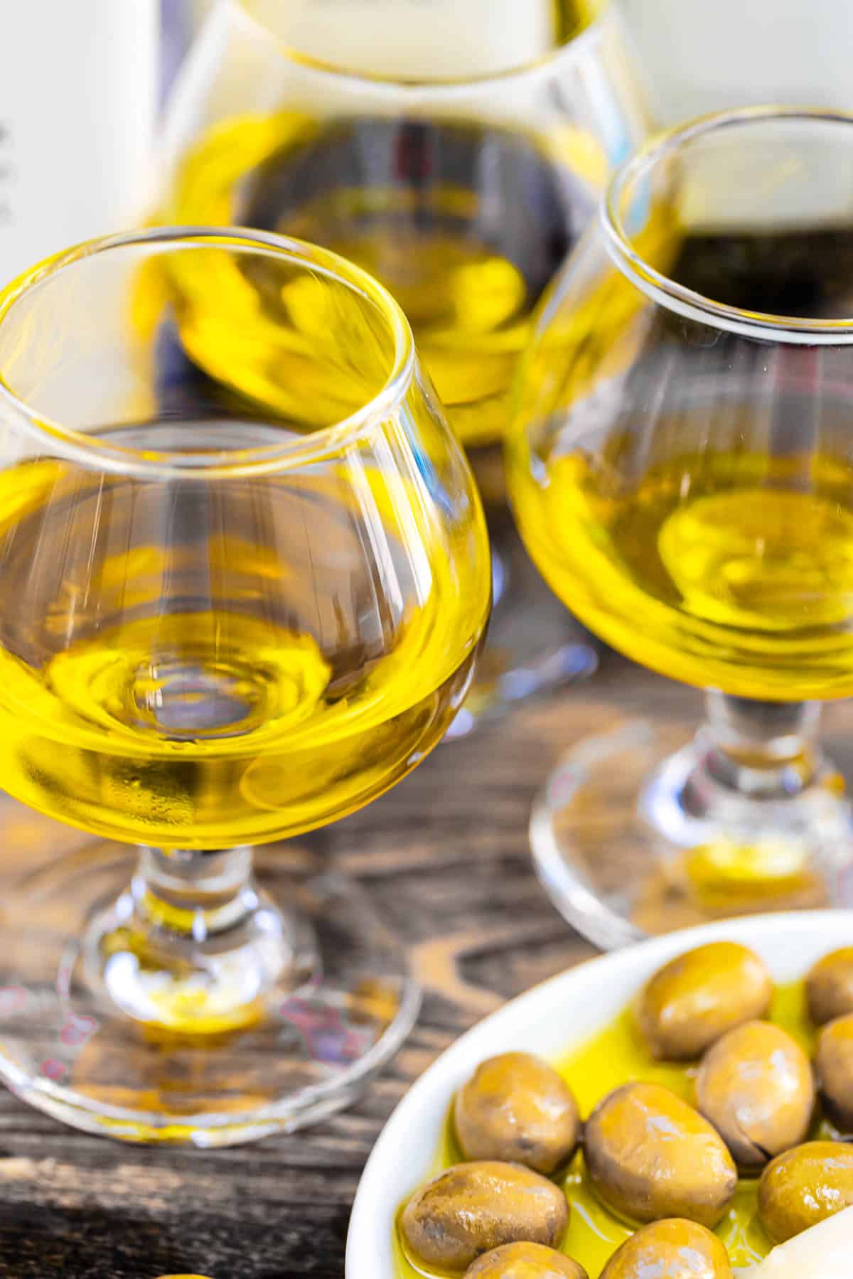 a close up of 3 glasses of olive oil next to a plate of green olives.