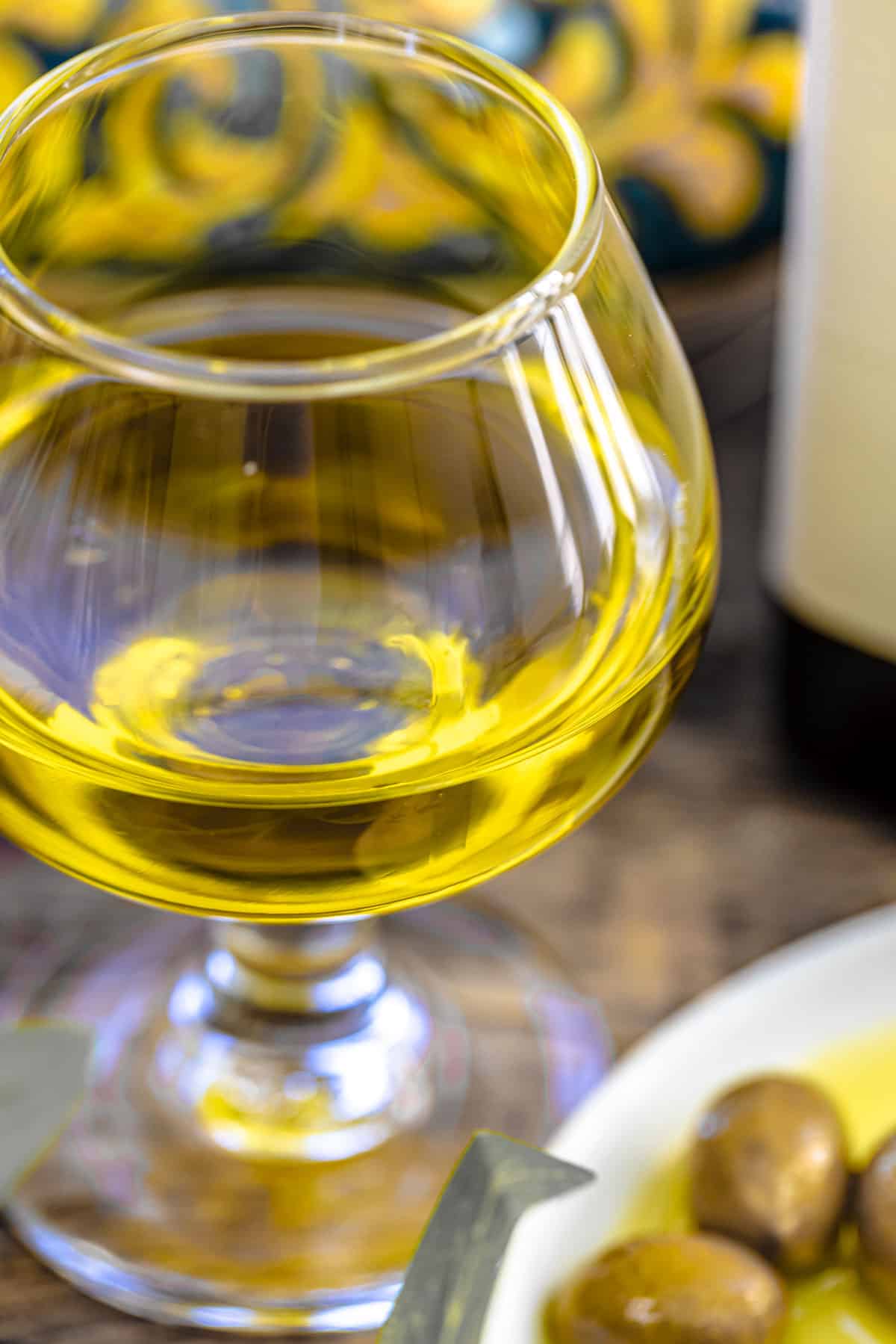 a close up of a small glass of olive oil and a plate of green olives.