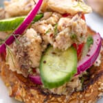 a close up of a sardine toast topped with cucumbers and pickled red onions.