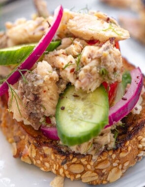 a close up of a sardine toast topped with cucumbers and pickled red onions.