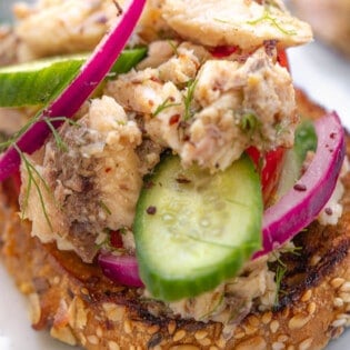 a close up of a sardine toast topped with cucumbers and pickled red onions.