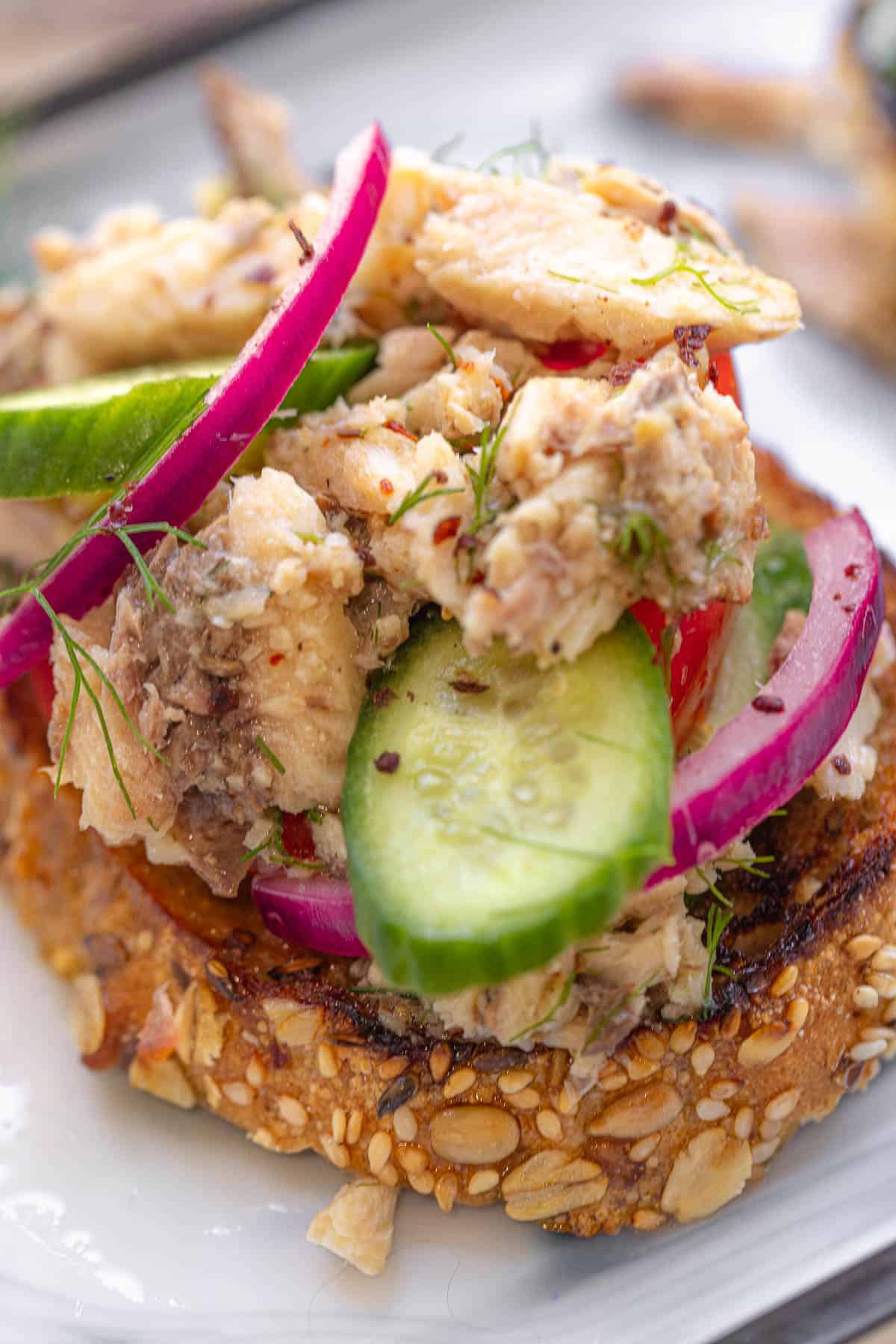 a close up of a sardine toast topped with cucumbers and pickled red onions.