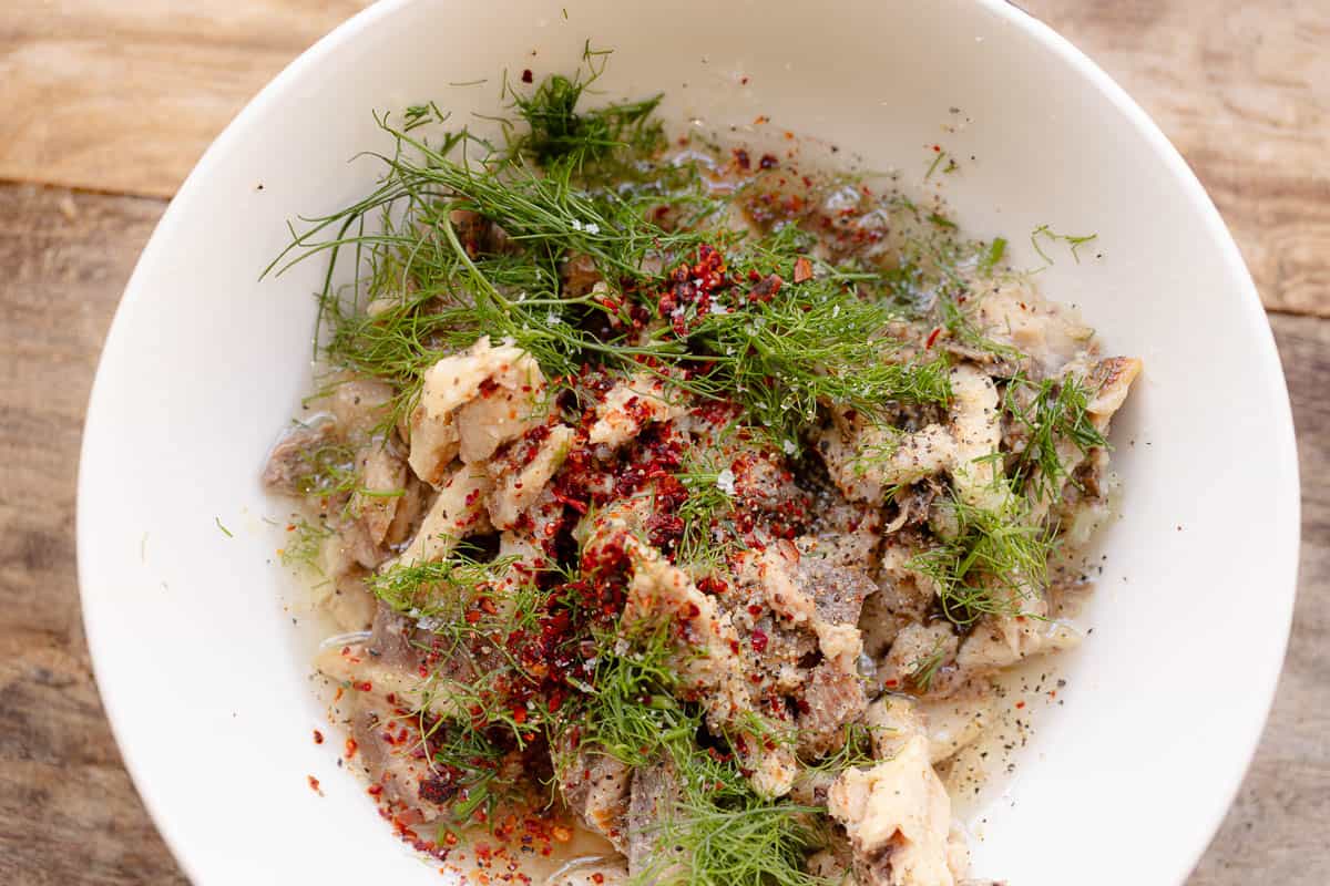 An overhead photo of the sardine mixture including sardines, parsley, aleppo pepper, lemon zest, lemon juice, salt, pepper and olive oil in a bowl.