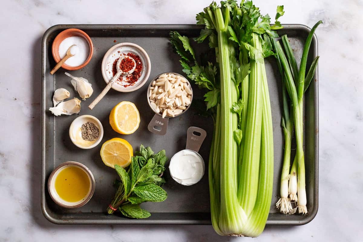 ingredients for celery salad including celery, greek yogurt, garlic, lemon juice, olive oil, aleppo pepper, salt, pepper, slivered almonds, scallions, and mint.