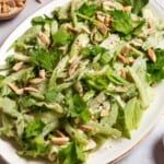 A close up of celery salad on a serving platter. Next to this are bowls of slivered almonds, aleppo pepper and a lemon half.