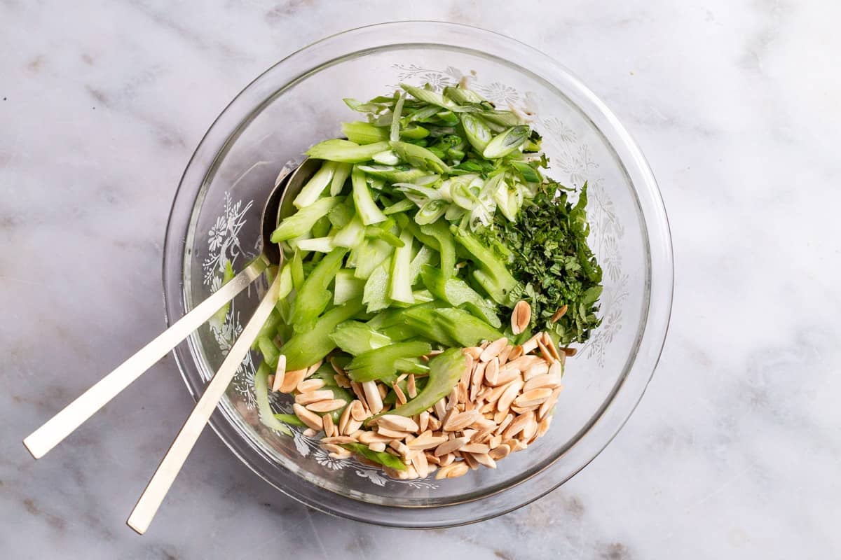 The ingredients for the celery salad in a bowl just before being mixed together with serving utensils.