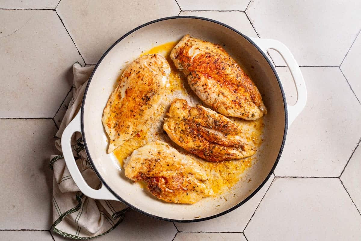 4 cooked chicken breasts in a skillet next to a kitchen towel.