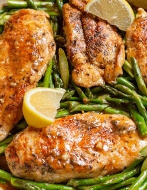 Chicken and asparagus in a skillet with lemon wedges.
