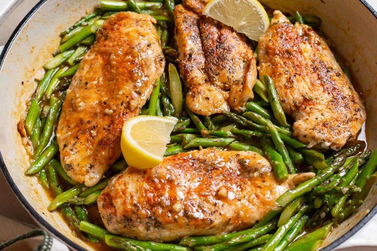 Chicken and asparagus in a skillet with lemon wedges.
