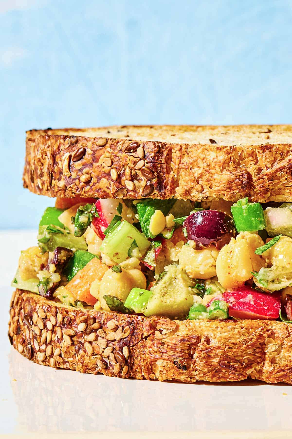 Close up of chickpea salad sandwich, showing the layers of fresh veggies, olives and more.