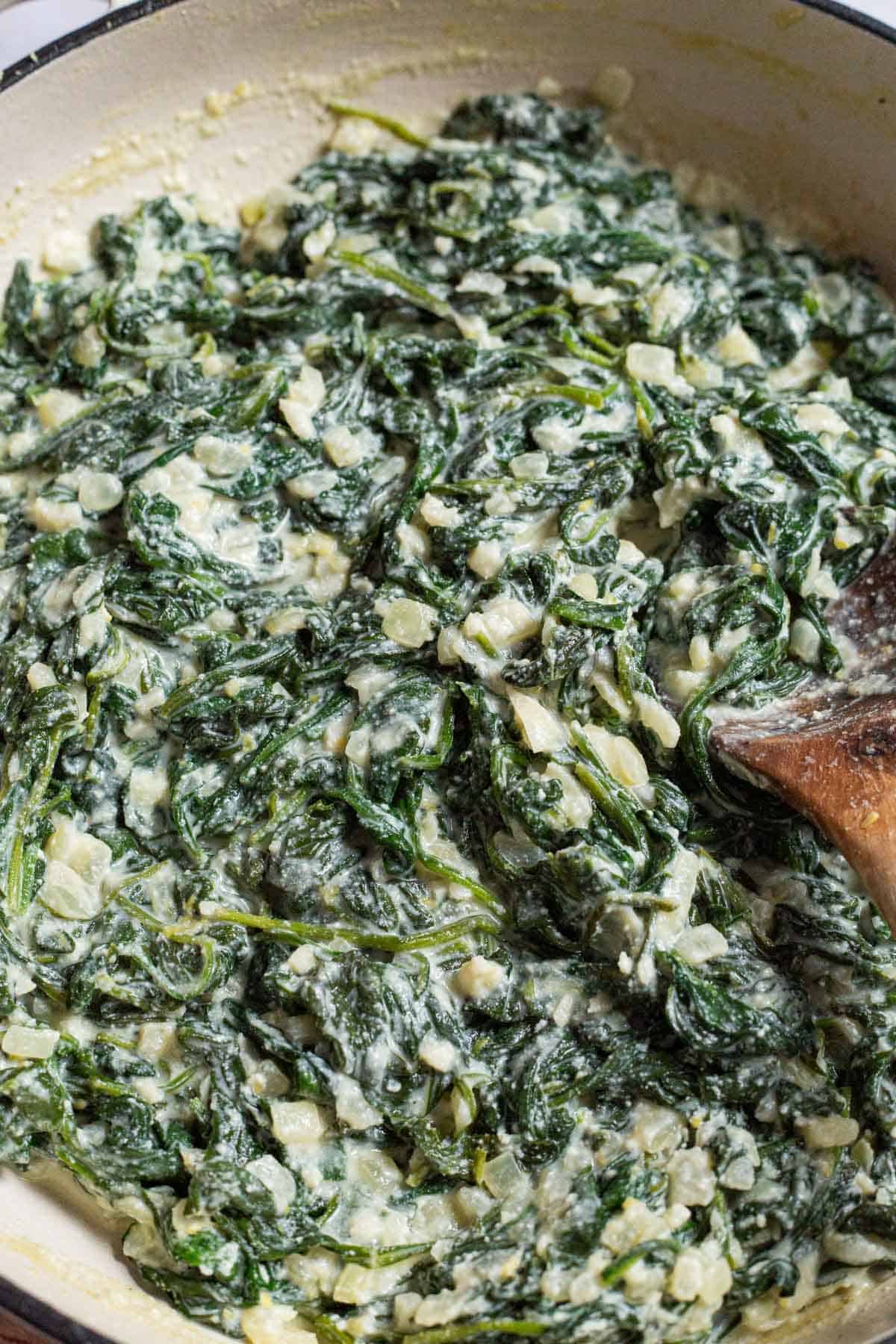 A close up of creamed spinach in a skillet with a wooden spoon.