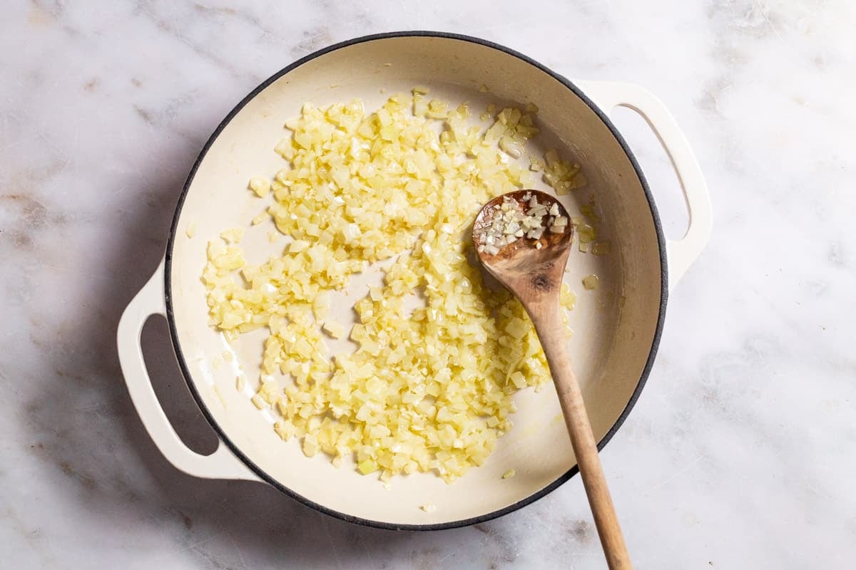 Chopped onions being sauteed in a skillet with a wooden spoon.