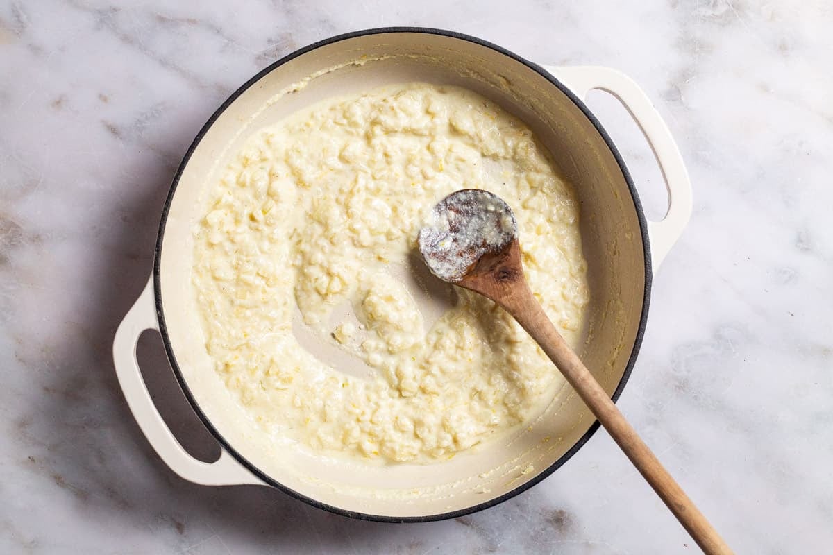 Sauce for the creamed spinach in a skillet being stirred with a wooden spoon.