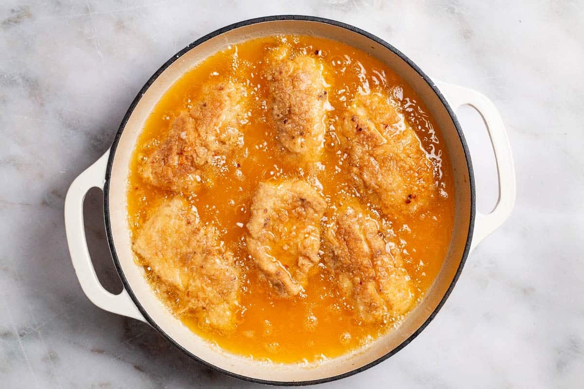 Fish fillets being fried in oil in a skillet.