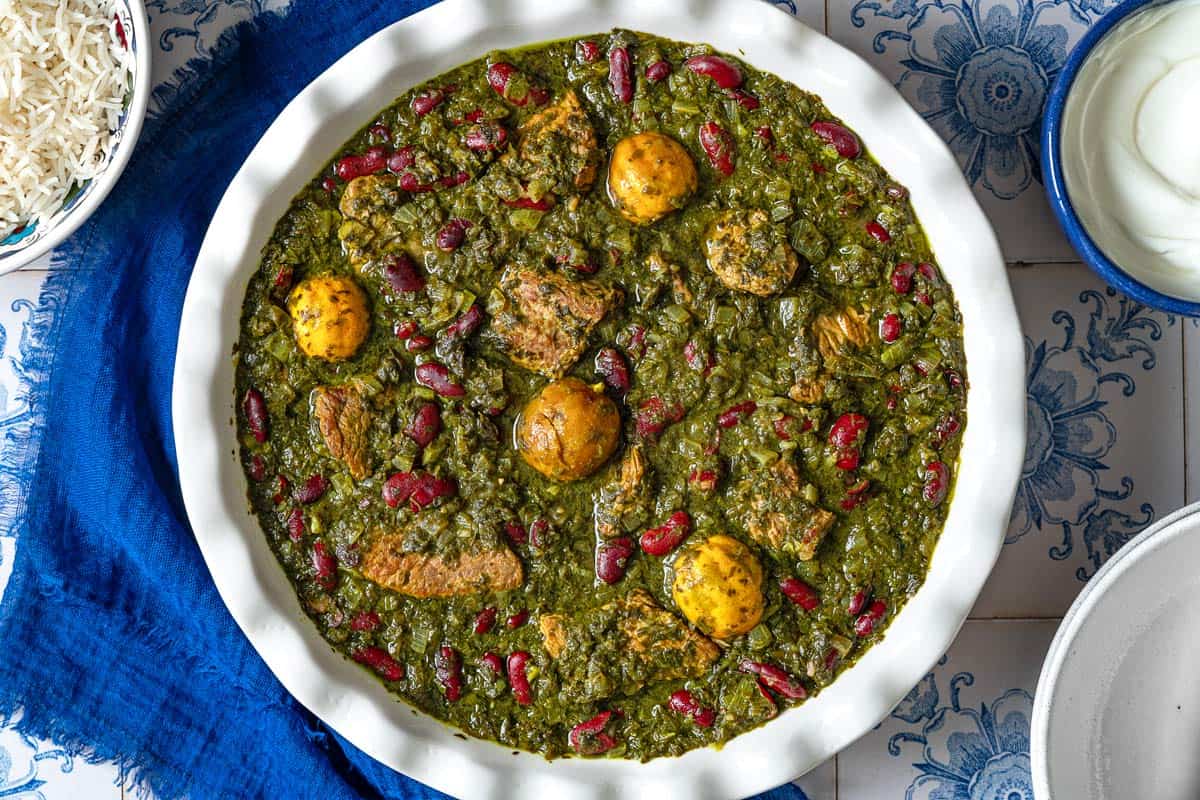 An overhead photo of ghormeh sabzi in a serving bowl. Next to this are bowls of rice and Greek yogurt.