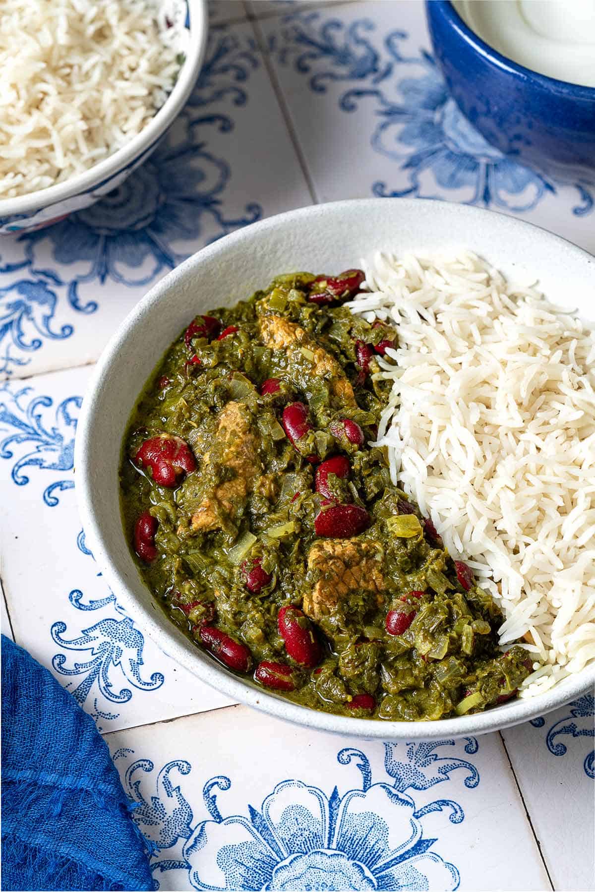 Ghormeh sabzi in a bowl with rice. In the background, there is another bowl of rice.