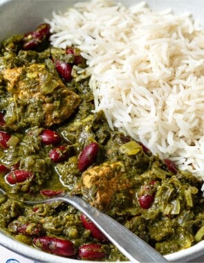 A close up of ghormeh sabzi in a bowl with rice and a spoon.