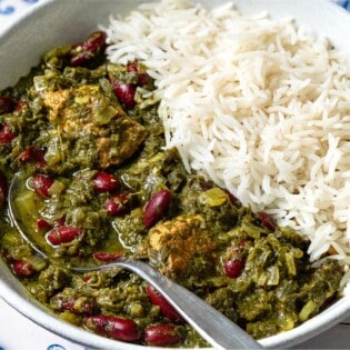 A close up of ghormeh sabzi in a bowl with rice and a spoon.