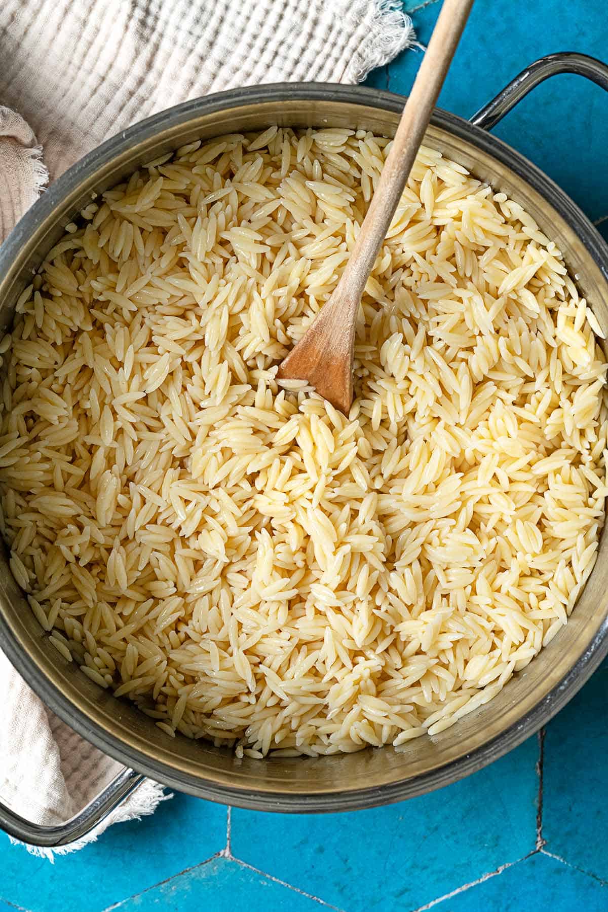 Cooked orzo in a large pot with a wooden spoon. Next to this is a cloth towel.