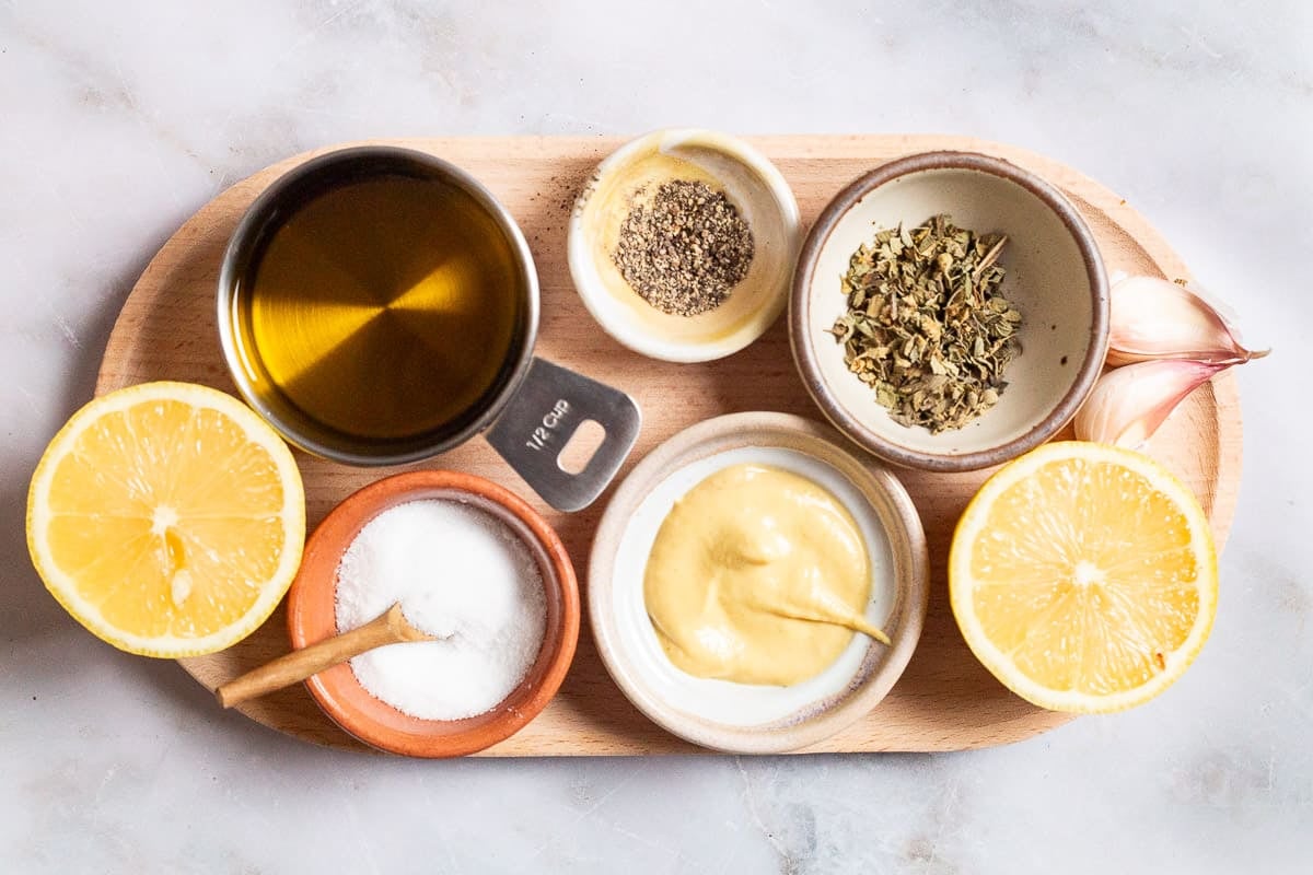 ingredients for a lemon vinaigrette recipe including lemon juice, dijon mustard, garlic, oregano, salt, pepper and olive oil.