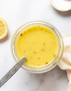 An overhead photo a jar of lemon vinaigrette with a spoon next to lemon halves, a small bowl of salt, and a cloth towel.