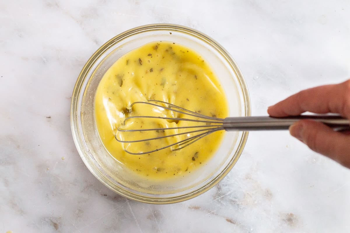 The ingredients for lemon vinaigrette being mixed together with a whisk.