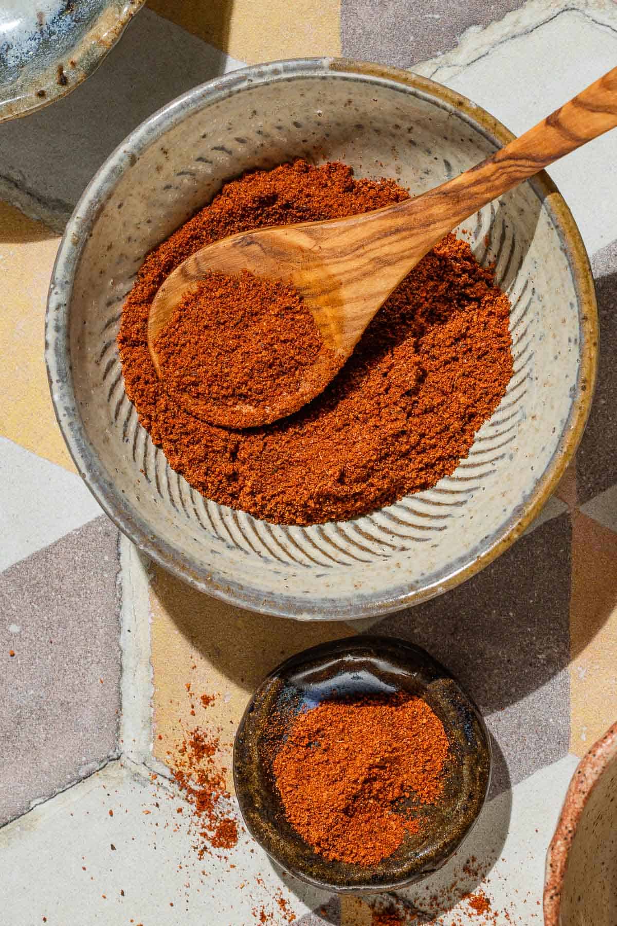 An overhead photo of baharat spice blend in a bowl with a small wooden spoon. Next to this is a small bowl of the spice.