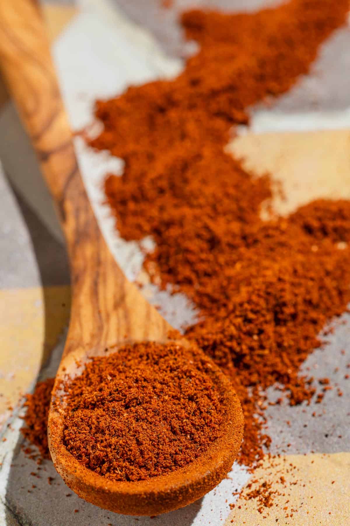 Baharat spice blend on a small wooden spoon next to more of the spice sprinkled around it.
