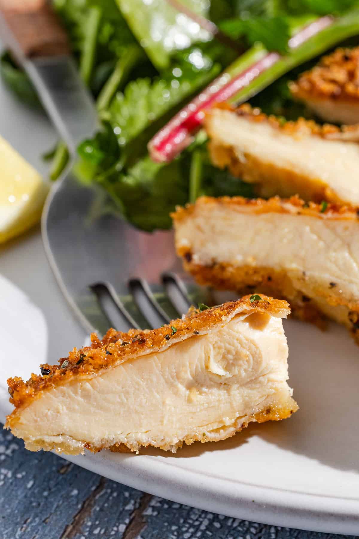 A close up of a sliced chicken cutlet on a plate with a fork.