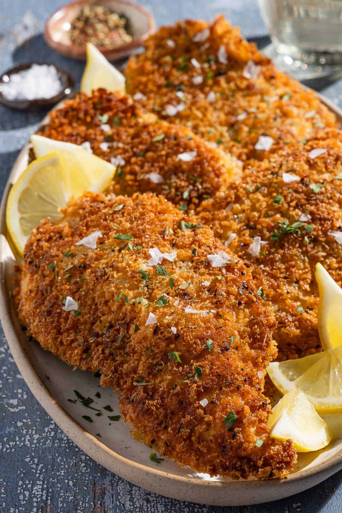 A close up of 4 chicken cutlets on a platter with lemon wedges.