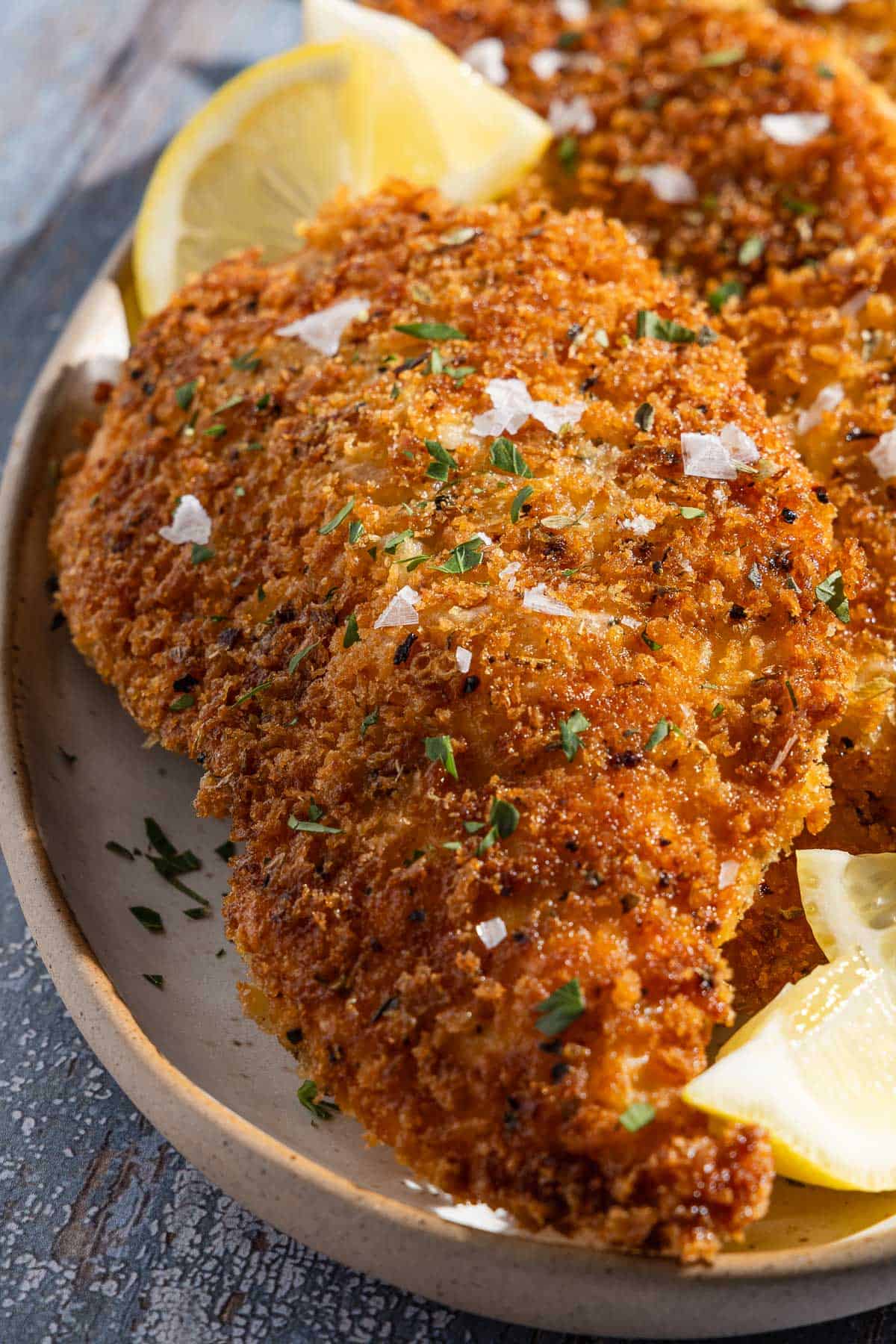 A close up of a chicken cutlet on a platter with lemon wedges.