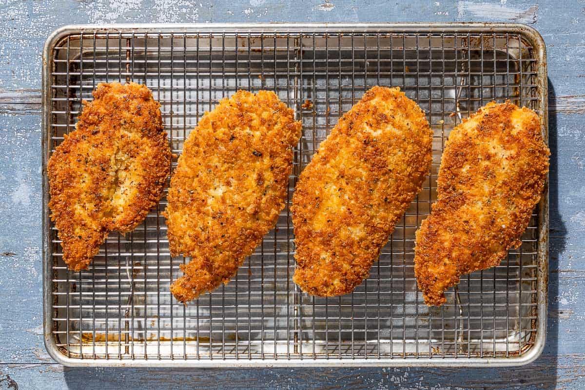 4 cooked chicken cutlets on draining on a wire rack placed over a cooking sheet.