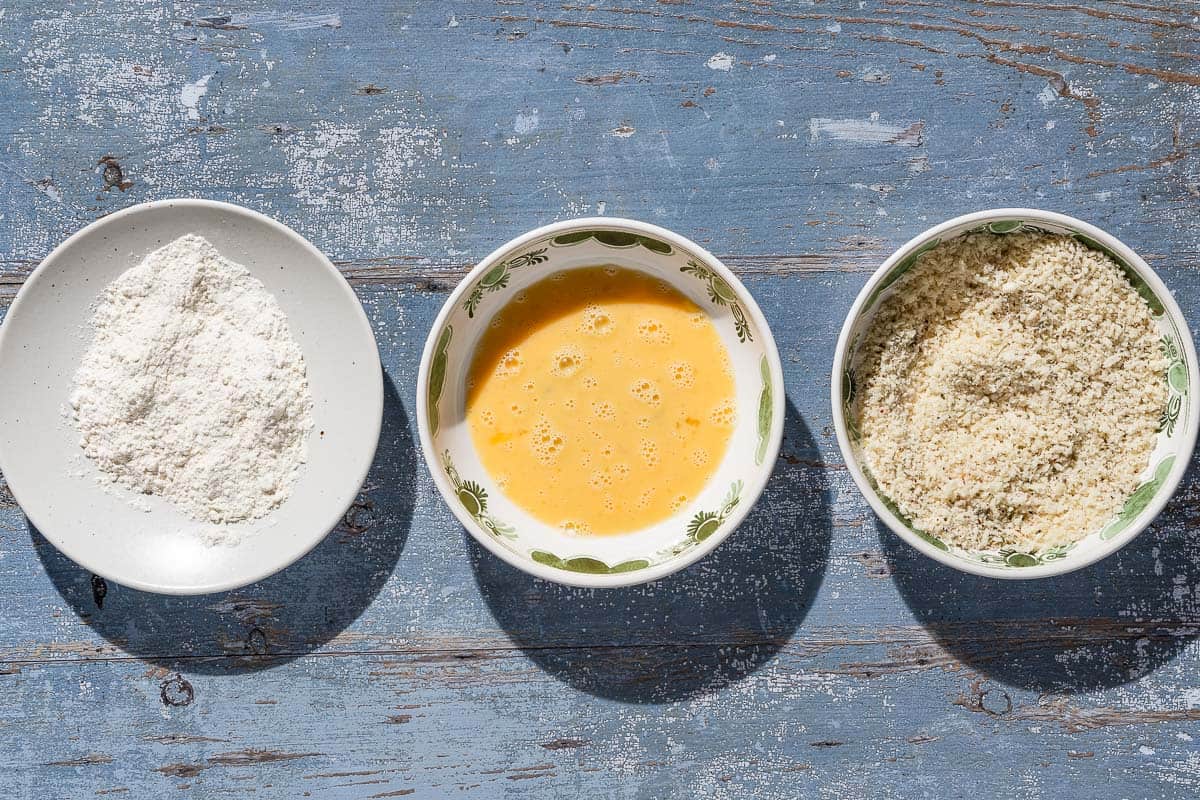 An overhead photo of a bowl of flour, a bowl of whisked eggs, and a bowl of breadcrumbs.