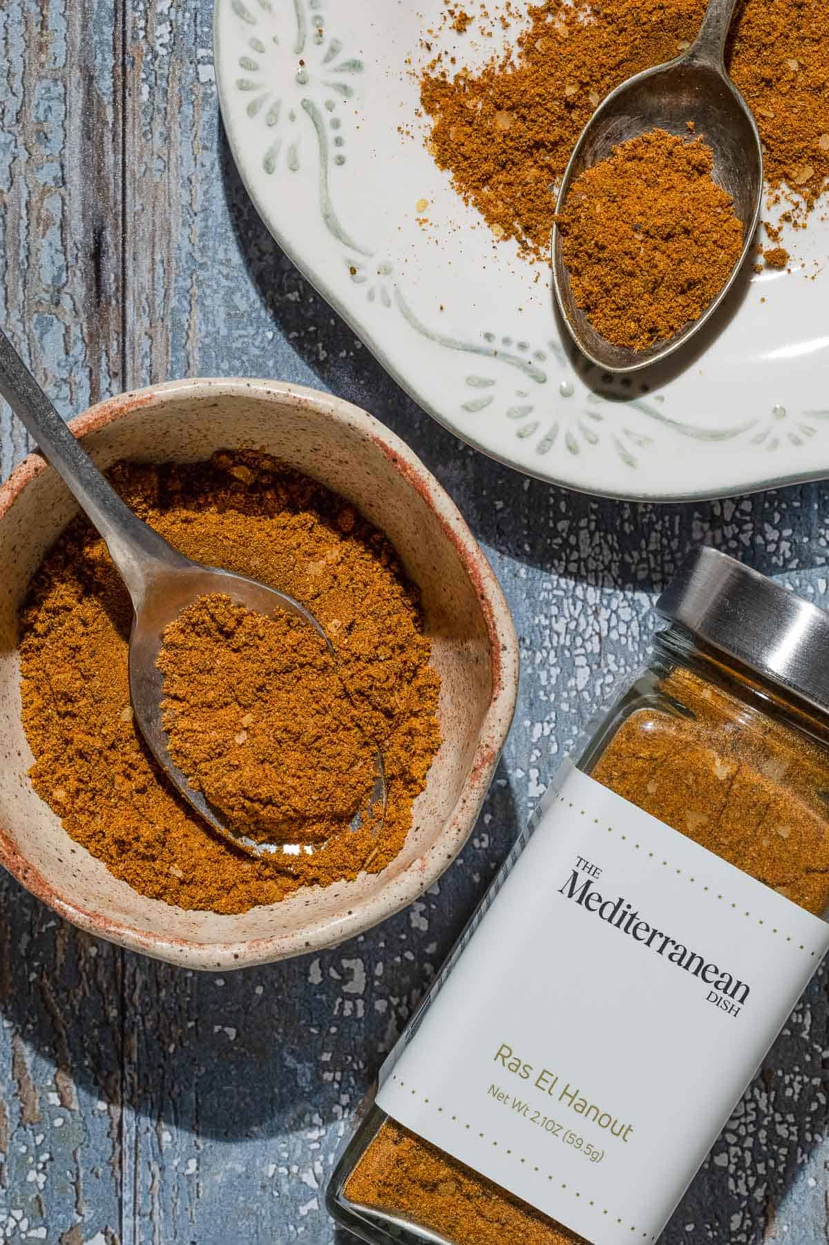 Ras el hanout on a plate with a spoon, in a bowl with a spoon, and a jar of the ras el hanout from the mediterranean dish.