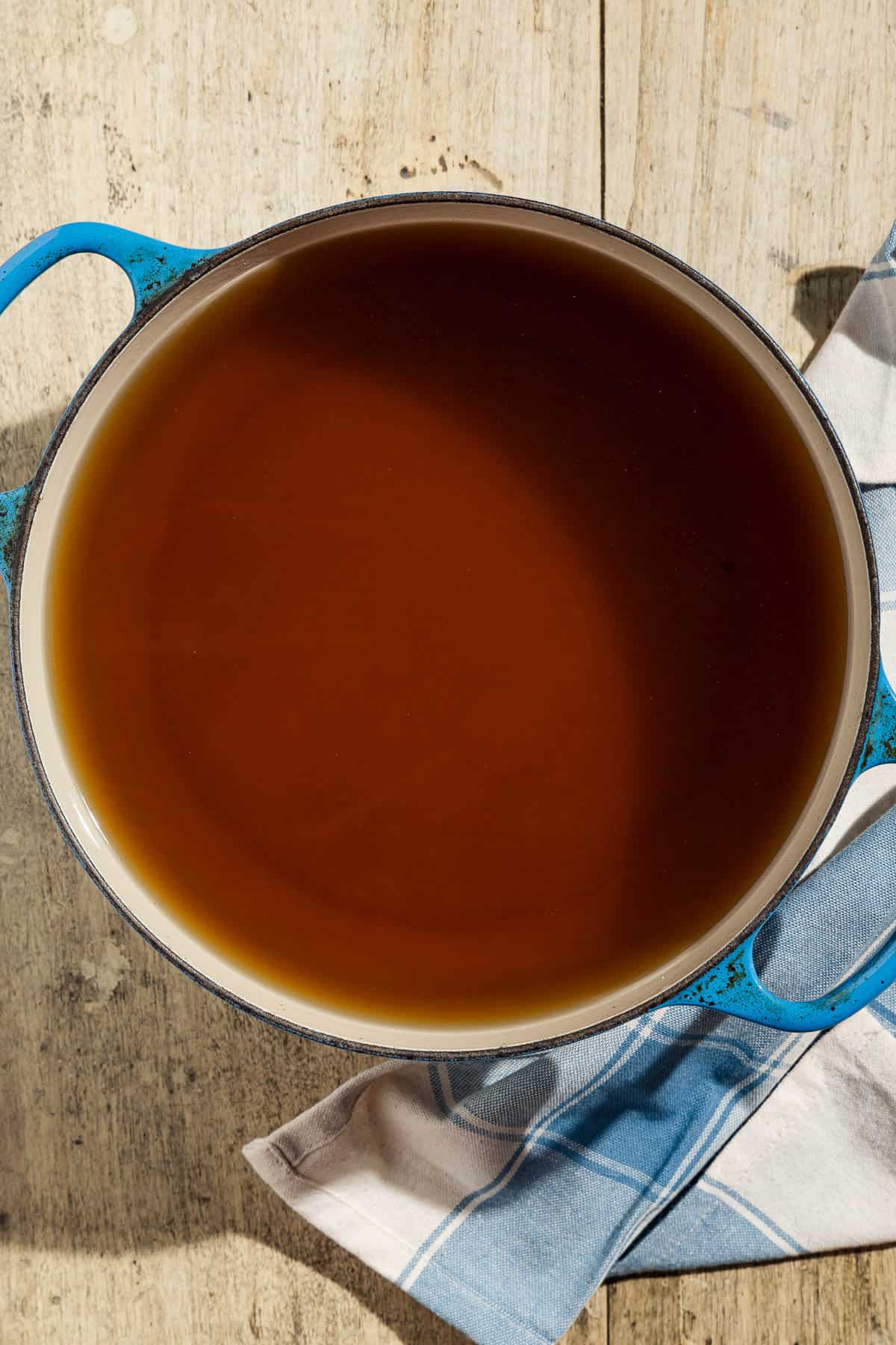 Homemade vegetable stock in a pot next to a kitchen towel.