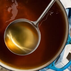 Homemade vegetable stock in a pot with a ladle next to a kitchen towel.