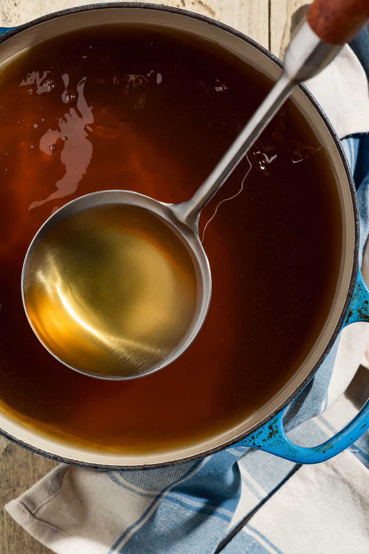 Homemade vegetable stock in a pot with a ladle next to a kitchen towel.