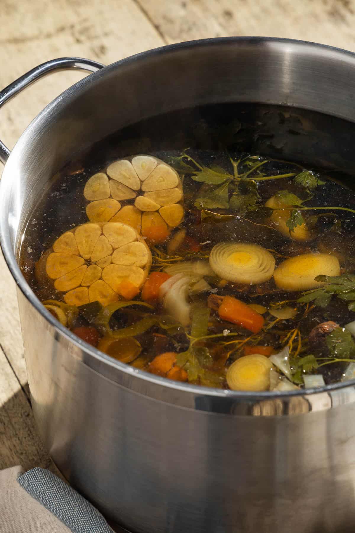 The ingredients for homemade vegetable stock simmering together in a large pot with water.