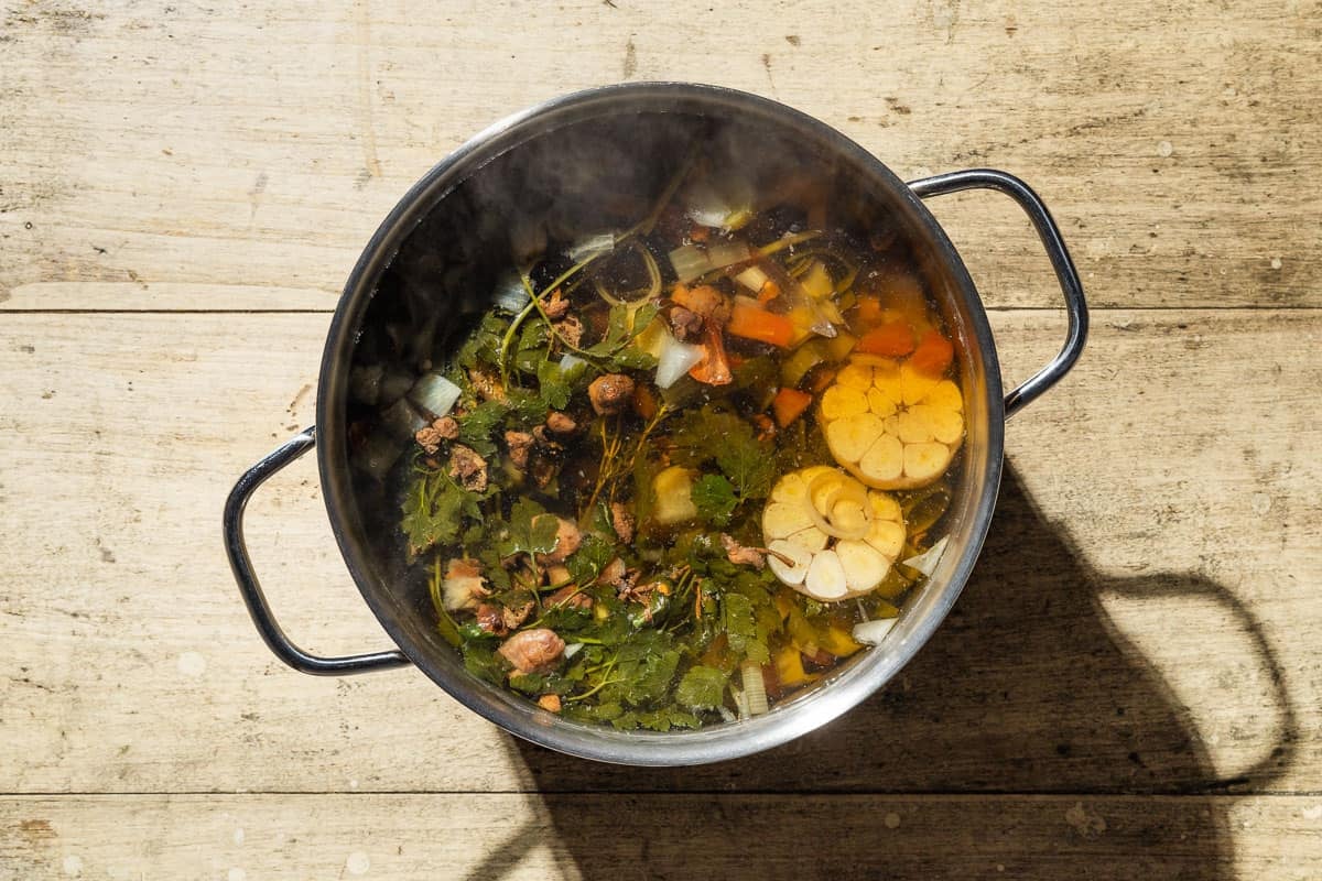 An overhead photo of the ingredients for homemade vegetable stock simmering together in a large pot with water.